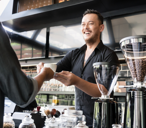 A server behind the cafe counter handing a cup of coffee to a customer